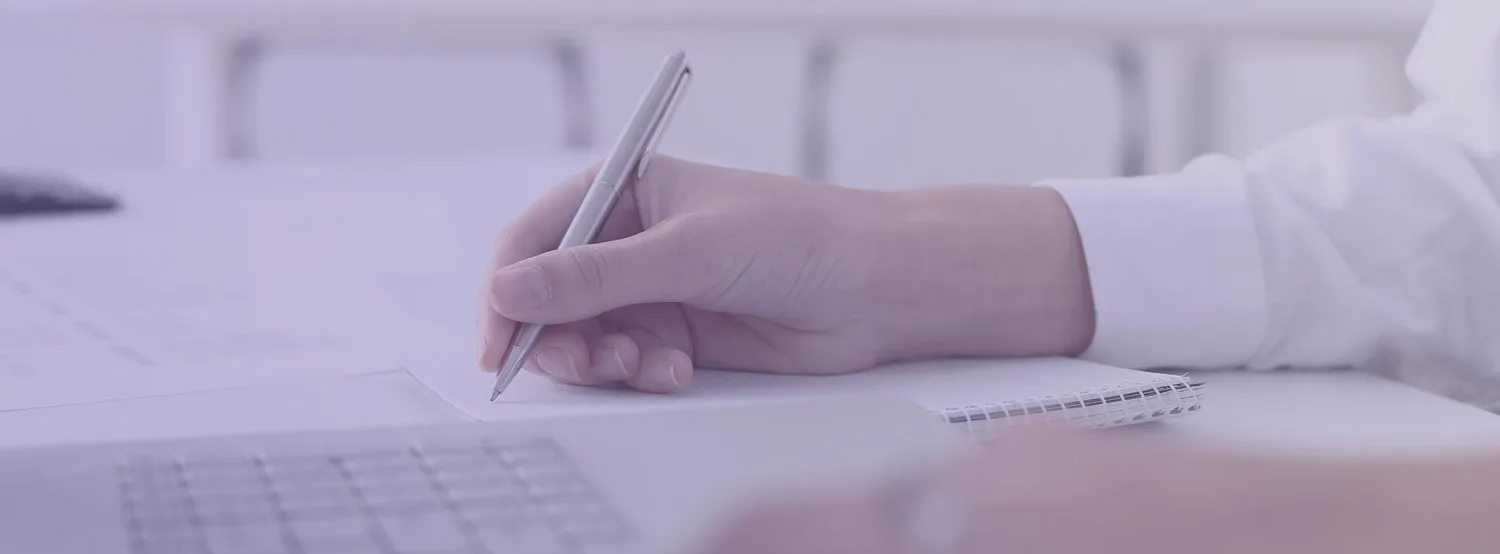 A hand holding a pen and listing resume skills on paper.