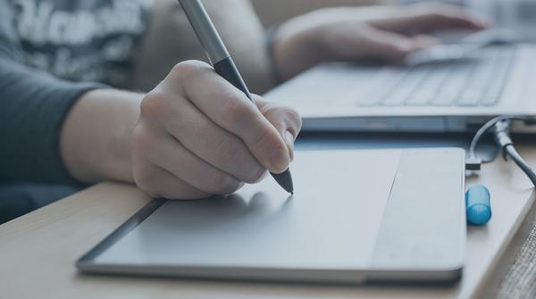 Hand with electronic pen on pad creating a Graphic designer CV.